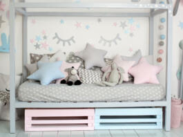 Interior of a children room with a wooden bed in shape of house. Home decor. A cozy Scandinavian style children bedroom with crafts,toys and cute pillows. Bedding and textiles for children nursery.