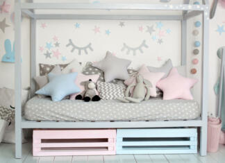 Kako izbrati pravo velikost otroške postelje in ležišča: Nasveti za udoben in varen spanec otroka Interior of a children room with a wooden bed in shape of house. Home decor. A cozy Scandinavian style children bedroom with crafts,toys and cute pillows. Bedding and textiles for children nursery.