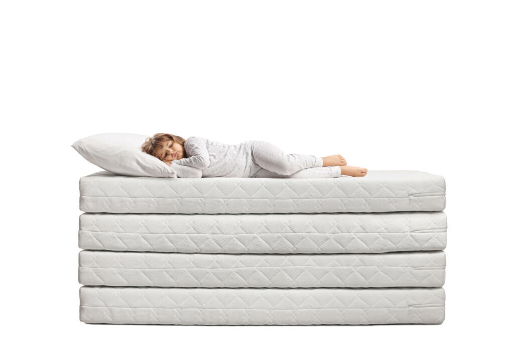 Little girl in pajamas sleeping over a pile of mattresses isolated on white background