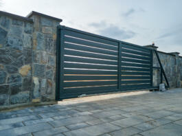 Wide automatic sliding gate with remote control installed in high stone fense wall. Security and protection concept.