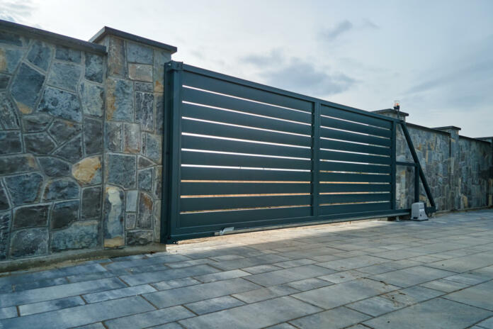 Wide automatic sliding gate with remote control installed in high stone fense wall. Security and protection concept.