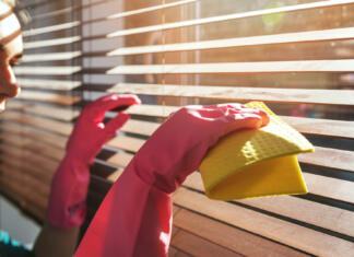 7 učinkovitih načinov za hitro čiščenje žaluzij woman cleaning wooden window blinds from dust at home on sunny day