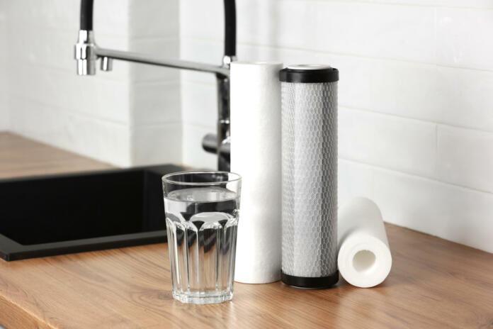 A glass of clean fresh water and set of filter cartridges on wooden table in a kitchen interior. Installation of reverse osmosis water purification system. Concept Household filtration system