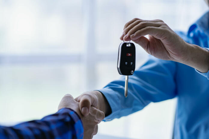 Closeup of car sale and buyer shaking hands Car salesman gives keys to buyer Close-up of car dealership business giving keys to new owner and handshake in office