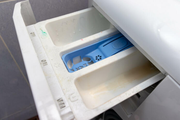 Dirty moldy washing machine detergent and fabric conditioner dispenser drawer compartment close up. Mold, rust and limescale in washing machine tray. Home appliances periodic maintenance.