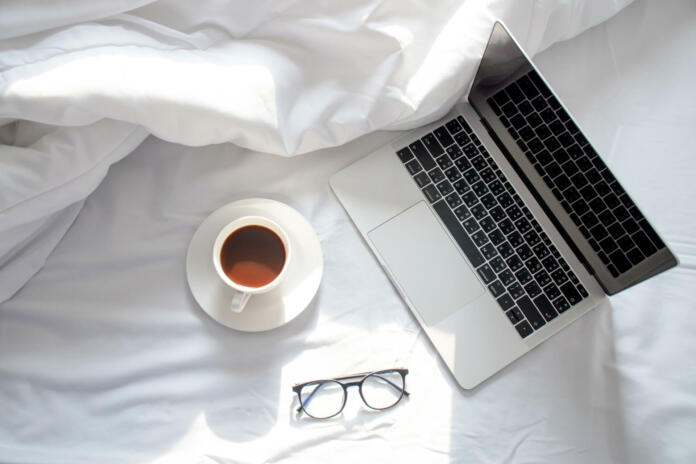 The morning sun shines on the laptop and coffee on the bed, the white sheet in the top view.