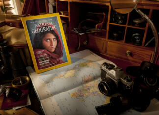 Konec National Geographica kot ga poznamo Alston, UK - July 2, 2011: A classic edition of the National Geographic magazine circa. 1985, lies on a wooden bureau surrounded by a selection of typical photo-journalist equipment including a Pentax K1000 35mm film camera, a Billingham 335 camera bag, a Philips Great World Atlas and several Optomax and Asahi camera lenses.