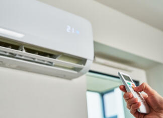 Kaj vse moramo vedeti pred nakupom klime v letu 2023? Hand adjusting temperature on air conditioner with remote control, Working air conditioner for comfort temperature in home at hot summer