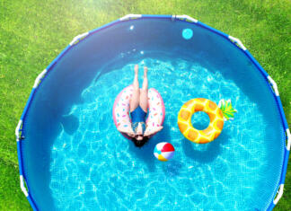 Nakup bazena od A do Ž: Vse, kar morate vedeti o nakupu bazena Aerial. Girl resting in a metal frame pool with inflatable toys. Summer leisure and fun concept. Frame pool stand on a green grass lawn. Top view from drone.