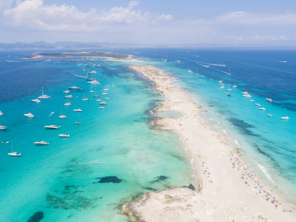 Aerial overhead view of large amount of yachts anchored off the coast of Formentera Ibiza, with turquoise Mediterranean Sea and ocean blue water.