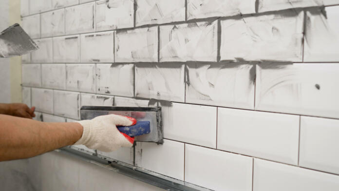 Black grout for white ceramic tiles. White tile in the kitchen with gray grout. The process of applying grout to ceramic tiles. Small ceramic tiles.