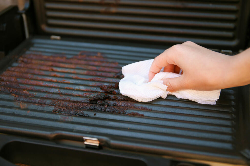 Dirty electric grill. Female hand wiping with cloth grill.