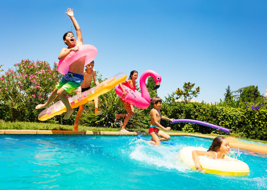 Group of age-diverse boys and girls, happy friends with swim floats jumping into swimming pool on the vacations