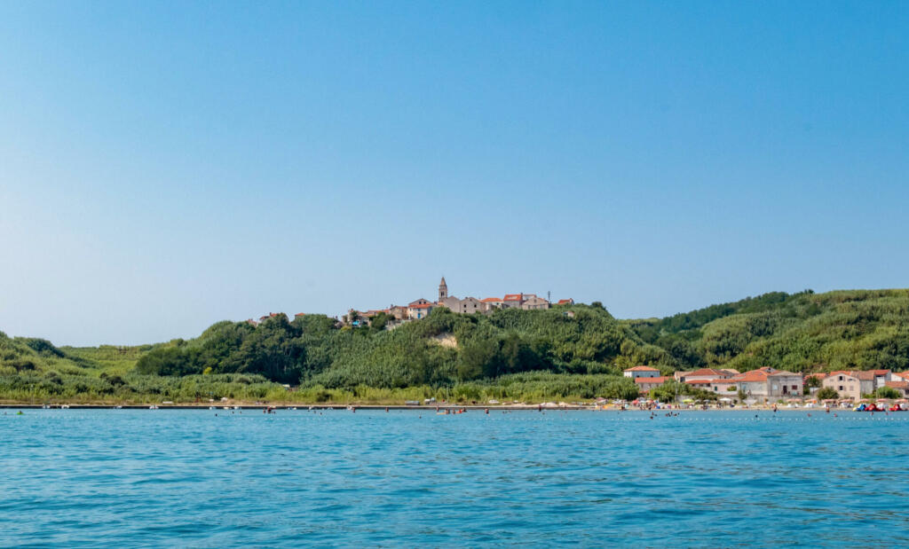 Idyllic small town on green island. Sea, summer, vacation, travel. People on beach on sunny day. Susak island, Croatia.