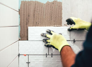 Izogibajte se teh 5 najbolj pogostih napak pri polaganju ploščic v kopalnici industrial construction worker installing small ceramic tiles on bathroom walls and applying mortar with trowel