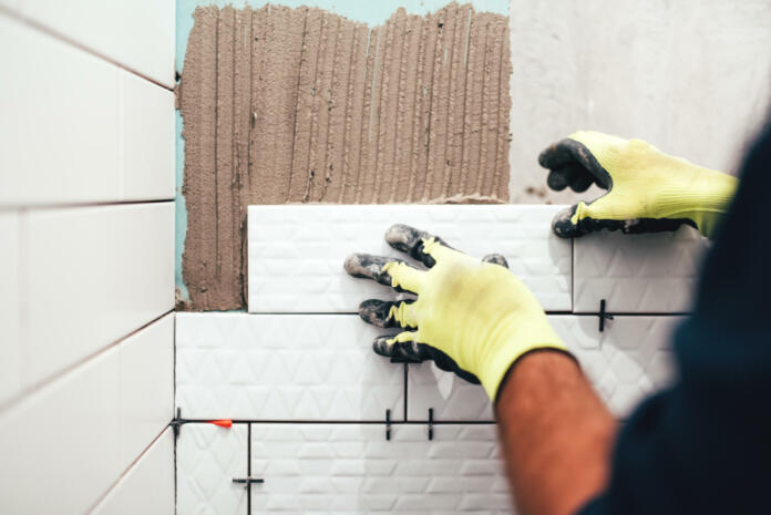 industrial construction worker installing small ceramic tiles on bathroom walls and applying mortar with trowel