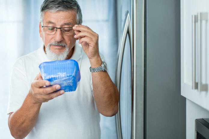 Is this still fine? Senior man in his kitchen by the fridge, looking at the expiry date of a product she took from her fridge -