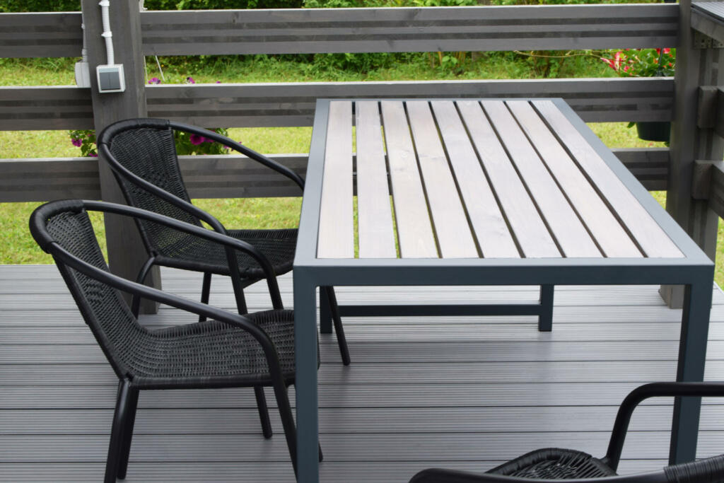 Plastic chairs and wooden table on WPC flooring terrace outdoors. Home outdoor terrace with empty patio furniture.