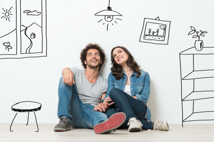 Portrait Of Happy Young Couple Sitting On Floor Looking Up While Dreaming Their New Home And Furnishing