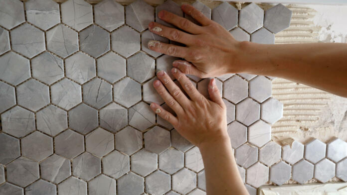 The master glues a mosaic of ceramic tiles. The worker presses the tile with his hands while gluing the tile. The working tiler mounts the tile on the wall, presses it with his hands.