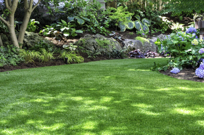 This beautiful backyard woodland garden features a maintenance free lawn made of realistic looking artificial grass, a huge landscaping trend for small spaces.