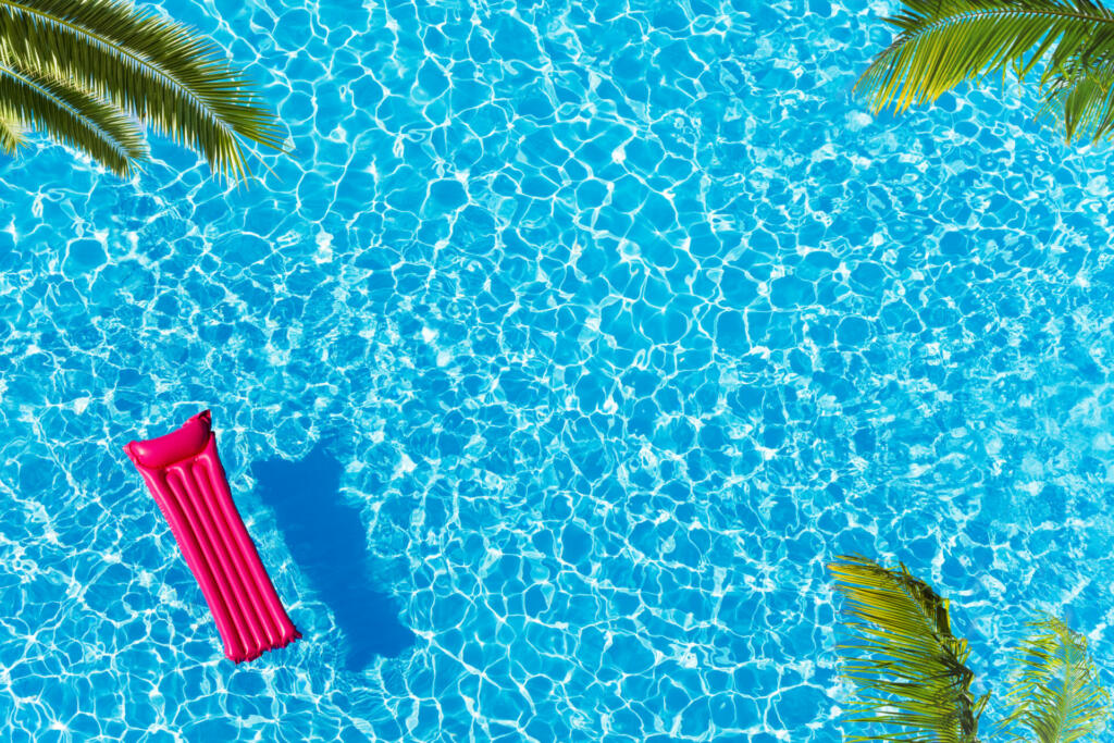 Vacation pool hotel view from above with ping matrass floating, water surface and palm trees