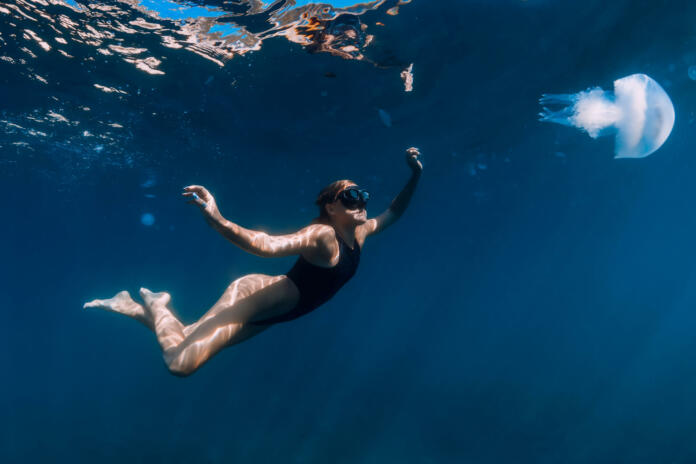 Woman underwater with jellyfish in blue ocean. Lady glides underwater in transparent sea