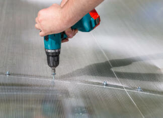 Kako zaščititi polikarbonatno kritino pred točo in podaljšati njeno življenjsko dobo Worker screwing screw into polycarbonate. Building greenhouse