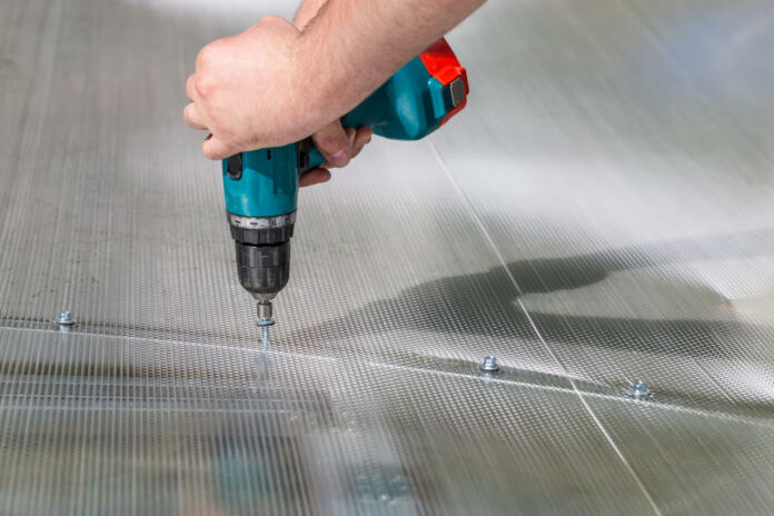 Worker screwing screw into polycarbonate. Building greenhouse