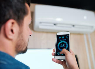 Prednosti in slabosti pametnih klimatskih naprav Young man with smartphone using smart application to adjust and support temperature of air conditioner