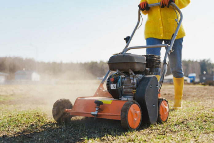 Young woman villager is using aerator machine to scarification and aeration of lawn or meadow