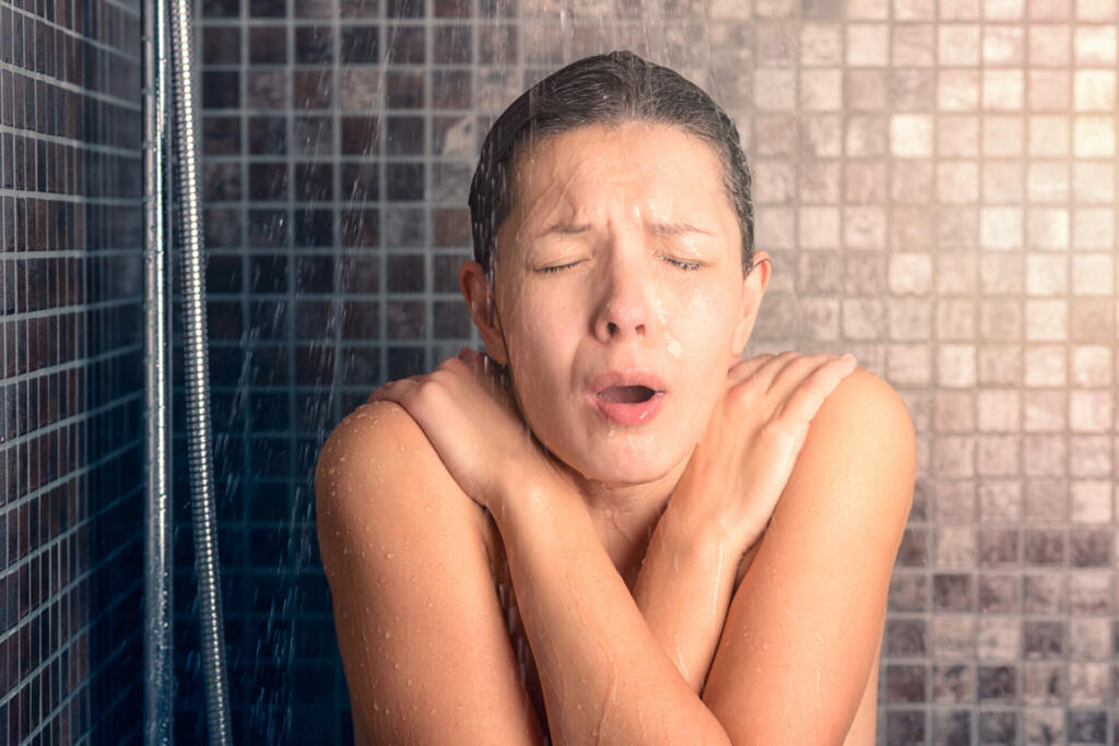 Close up Bare Young Woman Reacting While Taking Cold Shower with Arms Crossing Over her Chest and Eyes Closed.