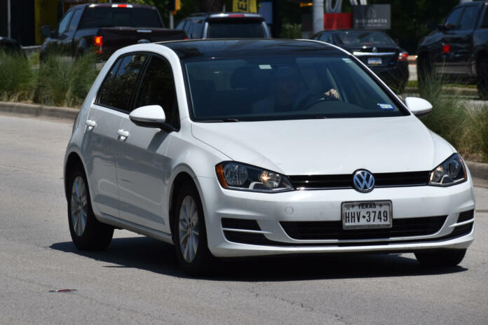 Houston, Texas USA 6-28-2023 - A white Volkswagen hatchback cruising on Allen Parkway in Houston