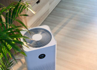 Lažje zadihajmo! 5 prednosti čistilcev zraka Air purifier on wooden floor in comfortable home. Fresh air and healthy life.