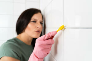 Close-up Of Person Hand Cleaning The Dirty White Tile Of The Wall Using Brush