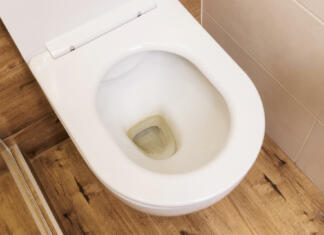 »Zvečer pred spanjem vlijem 50 g tega prahu v školjko, pokrijem in pustim tako čez noč« Close-up, top view, dirty unhygienic toilet bowl with lime yellow stain in the toilet. Modern apartment with a minimalist interior