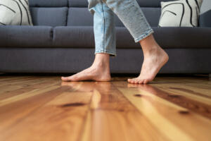 cropped shot of female legs walk barefoot on wooden warm floor near couch in living room at home, heating concept
