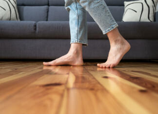 5 skritih prednosti električnega talnega ogrevanja cropped shot of female legs walk barefoot on wooden warm floor near couch in living room at home, heating concept
