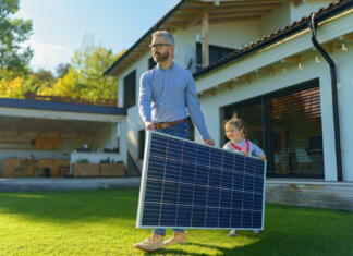 Rast rabe sončne energije v EU hitrejša od pričakovanega Father with his little daughter carring solar panel at the backyard. Alternative energy, saving resources and sustainable lifestyle concept.