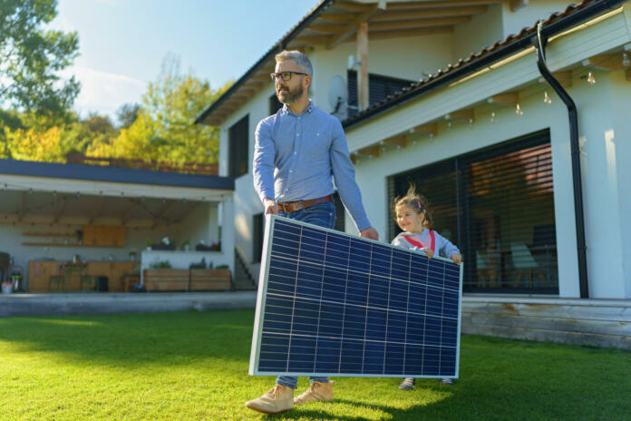 Father with his little daughter carring solar panel at the backyard. Alternative energy, saving resources and sustainable lifestyle concept.