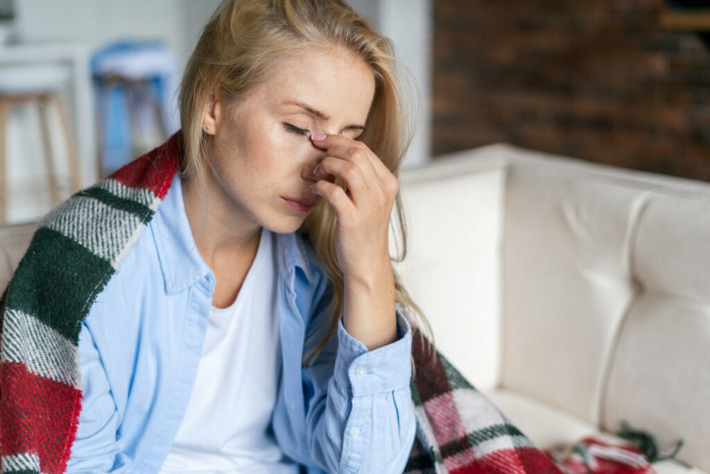 Fatigue and upset woman touching nose bridge feeling eye strain or headache, trying to relieve pain. Sick and exhausted female spending day at home. Depressed lady feeling weary dizzy