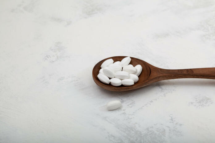 Pills Natural sugar substitute in wooden spoon, close-up. Selective focus. Sweetener as food additive used with drinks for diabetes and weight loss. Low carb diet.