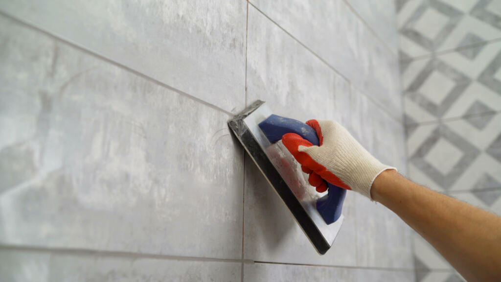 Seam grouting with black grout. Tile grout. Construction work with ceramic tiles. Grouting, joining wall tiles. The builder processes the seams between ceramic tiles.