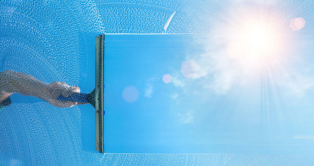 window cleaner cleaning window with squeegee and wiper on a sunny day