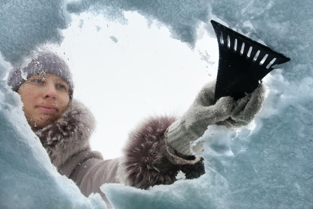 woman cleaning snow-covered car with a scraper