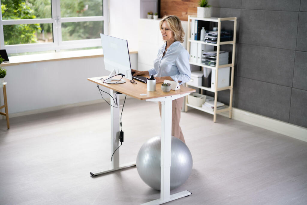 Woman Using Adjustable Height Standing Desk In Office For Good Posture