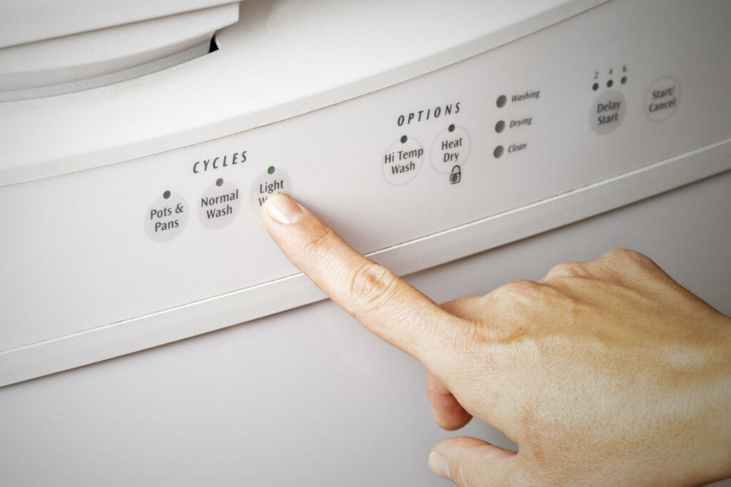 A woman's hand setting the dishwasher cycle to light wash, energy efficient concept