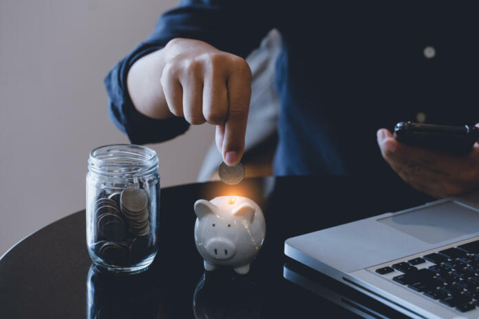 Businessman hand putting money coin into piggy and saving money concept.