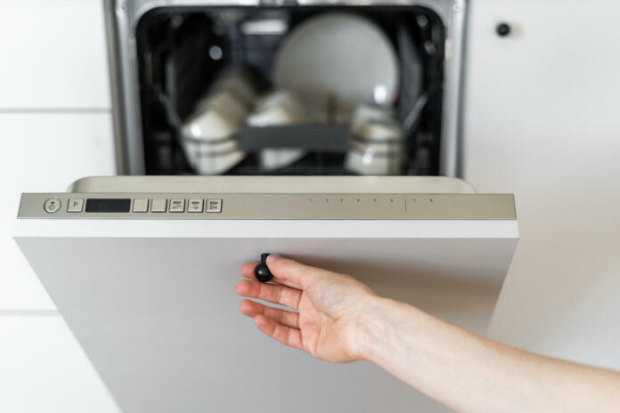 Cropped view of person's hand closing dishwasher with dirty utensils. Contemporary kitchen appliances. Home comfort. Concept of cleanliness. Kitchen interior design details