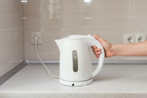 Electric Kettle in hand on the background of the kitchen.